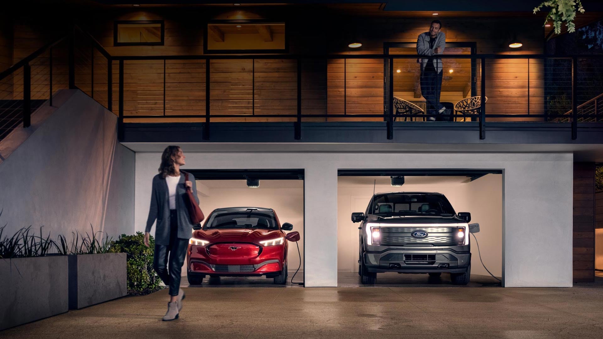 Woman walking out from home garage with a 2024 Mustang® Mach-E and Ford Lightning® truck in plugged-in and charging | Tipton Ford in Nacogdoches TX